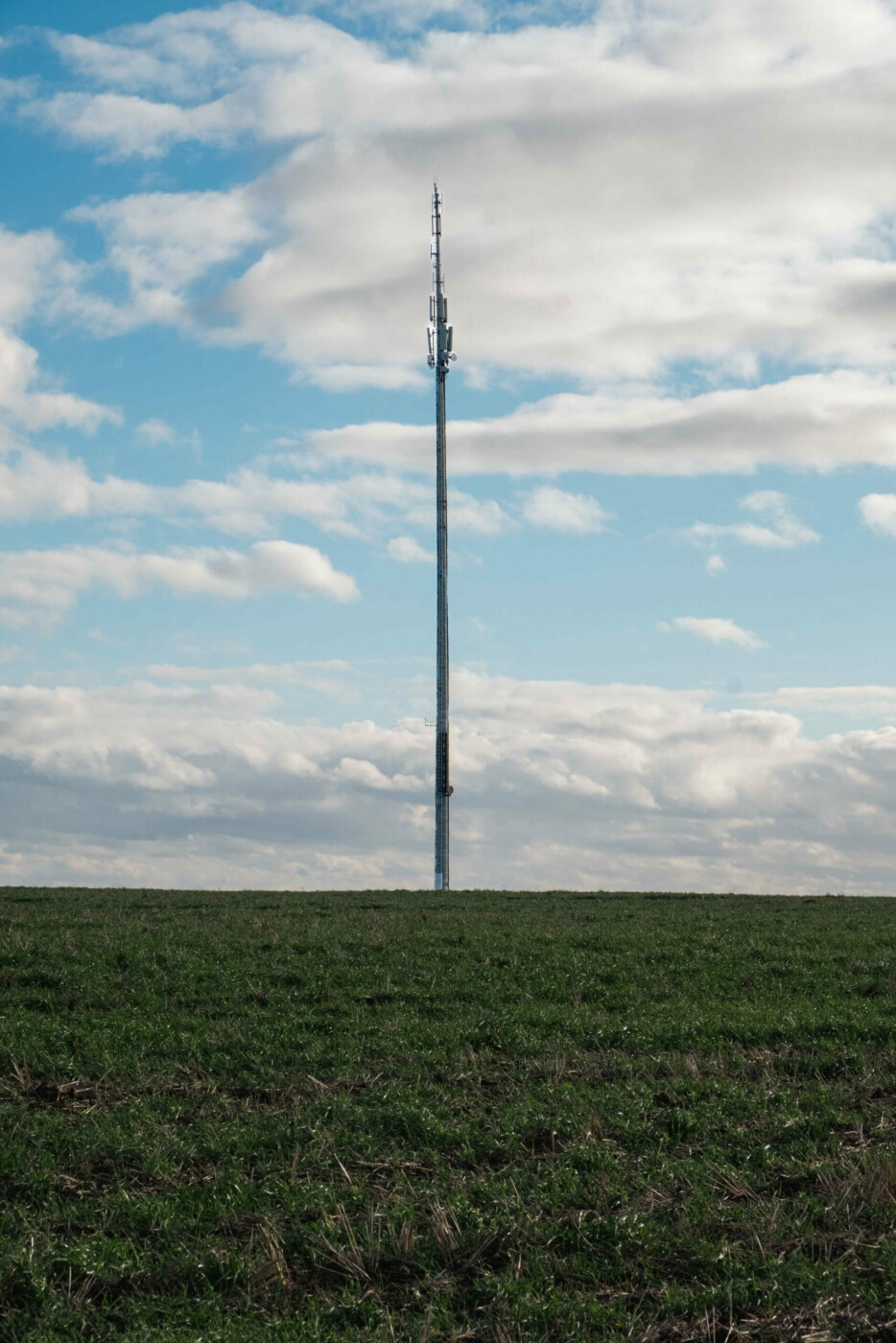 5G-Funkmast mitten im nirgendwo nur umgeben von Wiese und Wolken am Himmel.